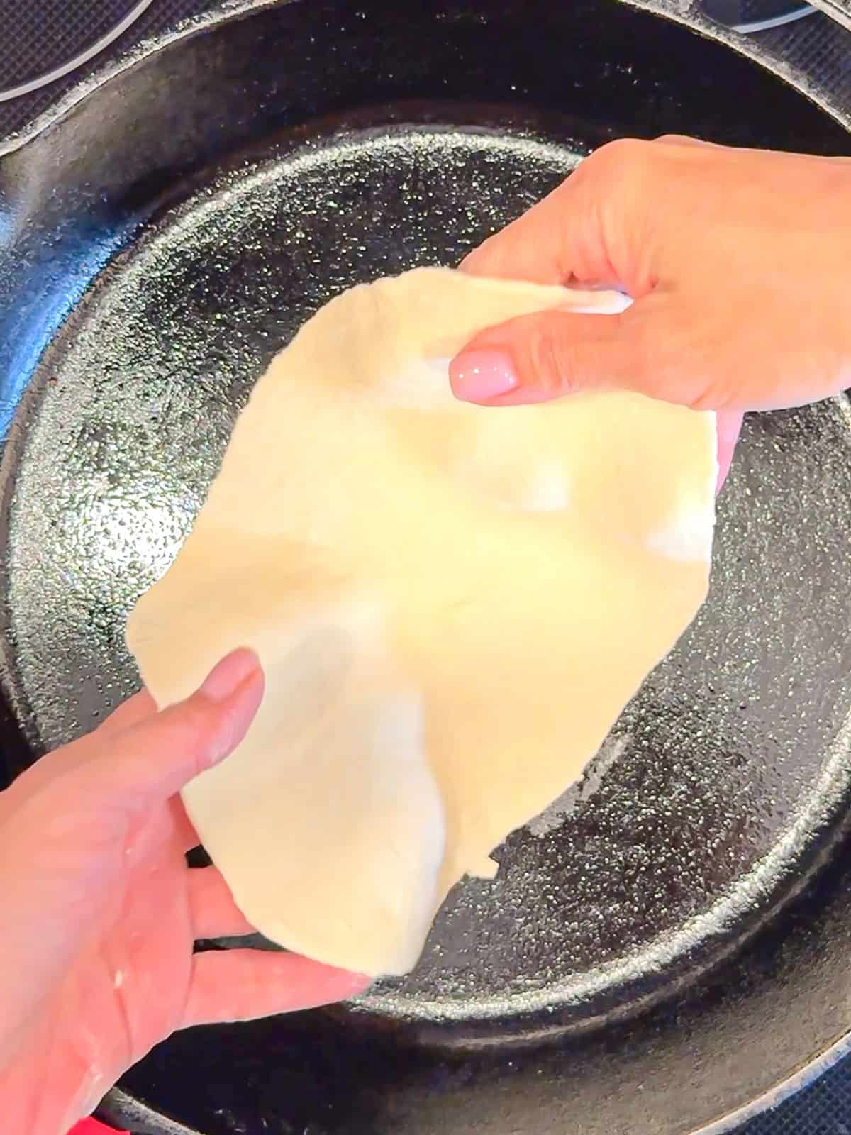 Placing flatbread dough into a cast-iron pan.