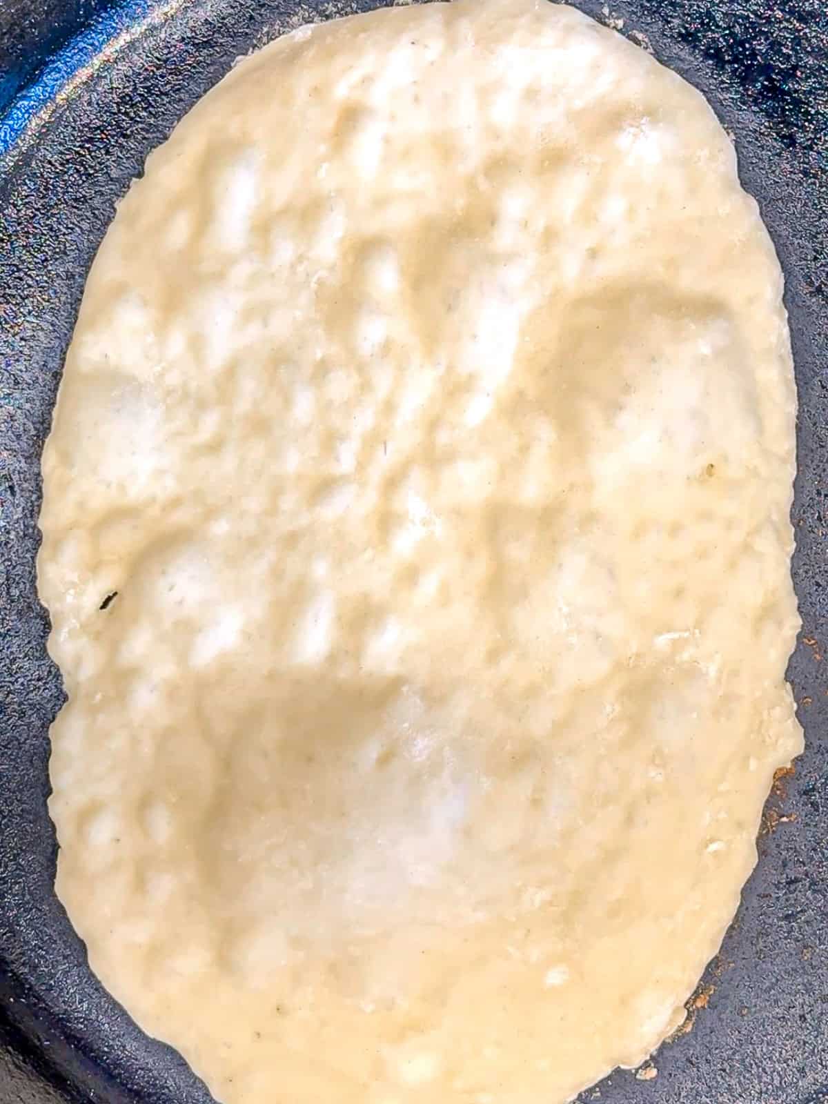 Showing the bubbles forming on the surface of two ingredient flatbread cooking in a cast-iron pan.