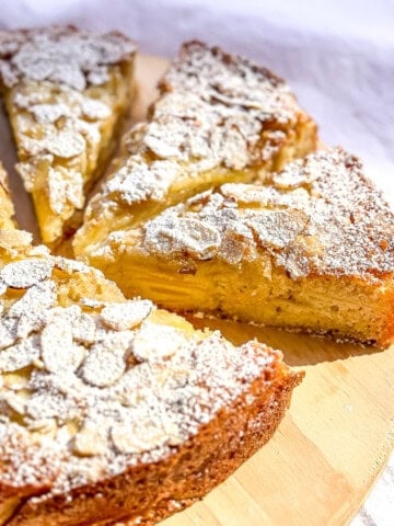 A sliced almond apple cake on a wooden cutting board.