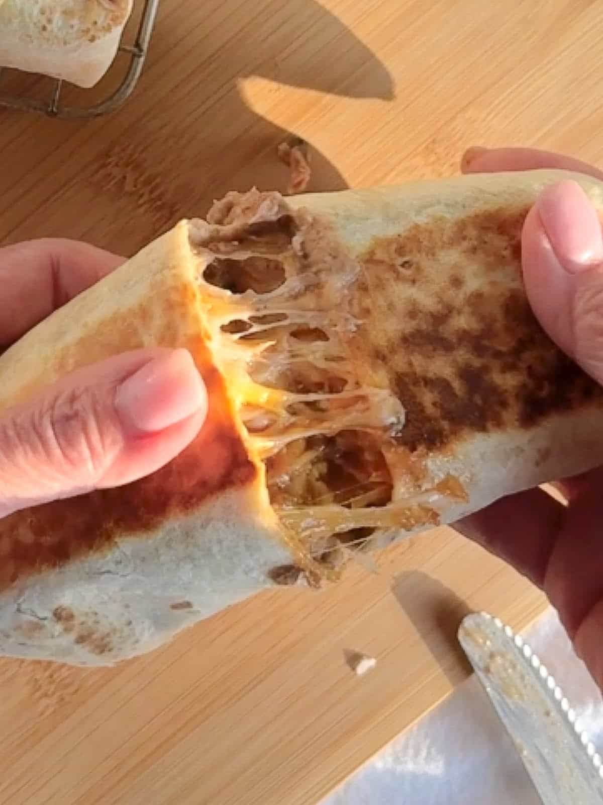 Cut view of a bean and cheese burrito, showing the melted cheese pull.