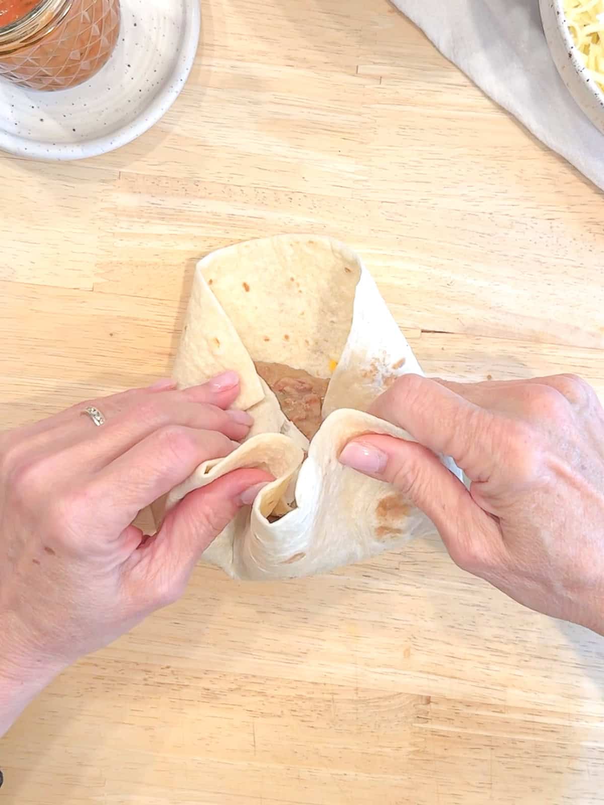 Rolling the bottom of the tortilla over the bean and cheese filling for a burrito.