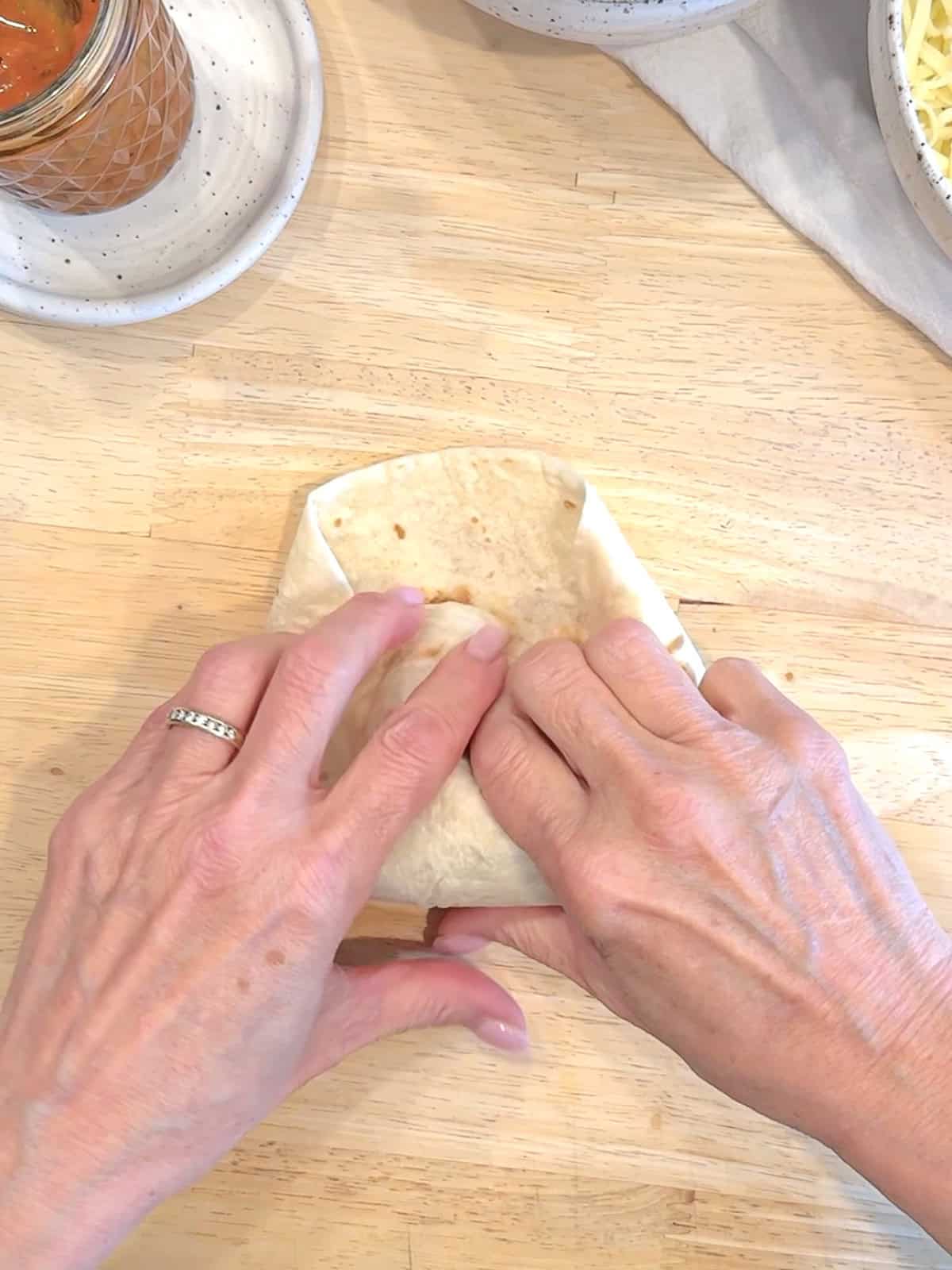 Pulling the bottom of the tortilla completely over the bean and cheese filling, pulling back to enclose it.