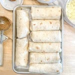 Rolled bean and cheese burritos on a sheet pan.