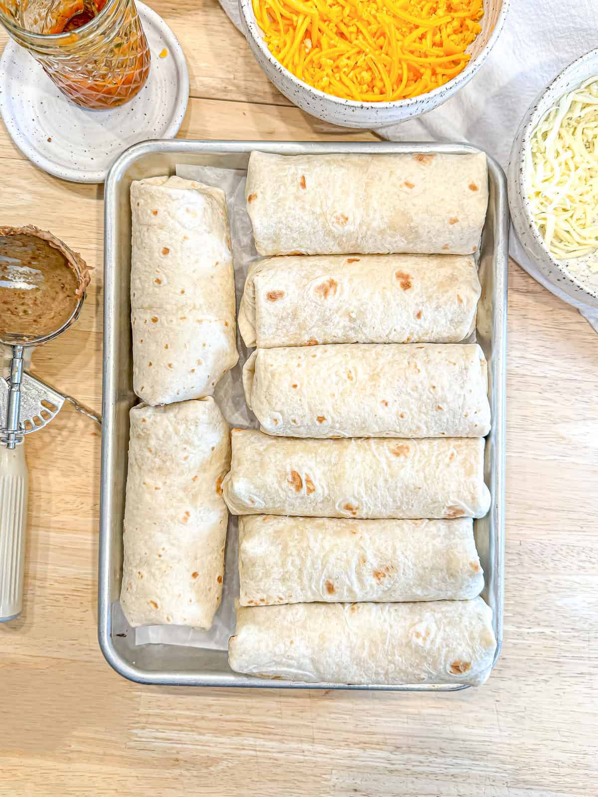 Rolled bean and cheese burritos on a sheet pan.