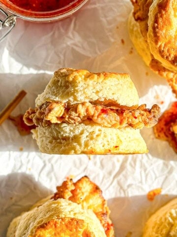 Side view of a fried chicken biscuit with spicy honey butter on parchment paper.