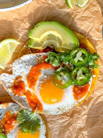 Huevos rancheros on parchment paper with accompanying garnishes.