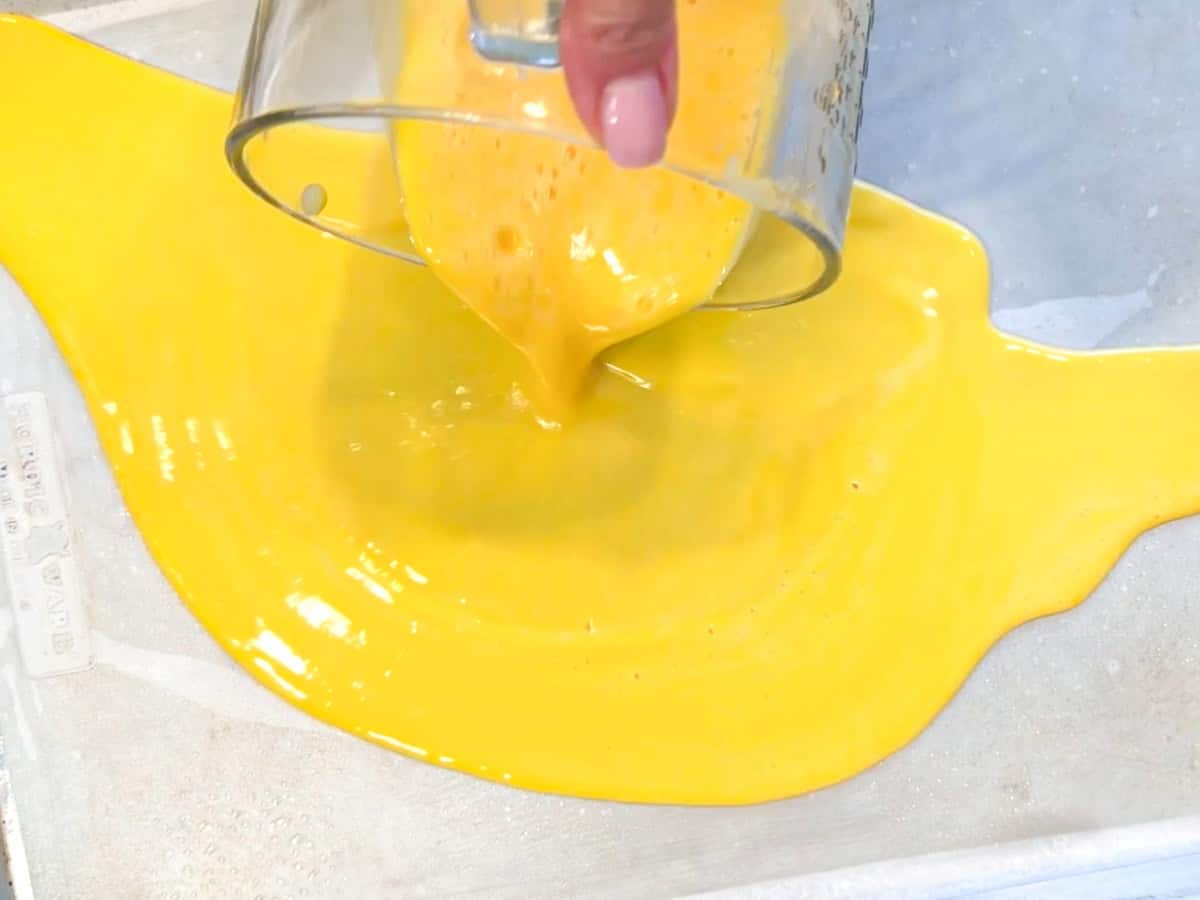 Pouring eggs into a sheet pan with a measuring cup.