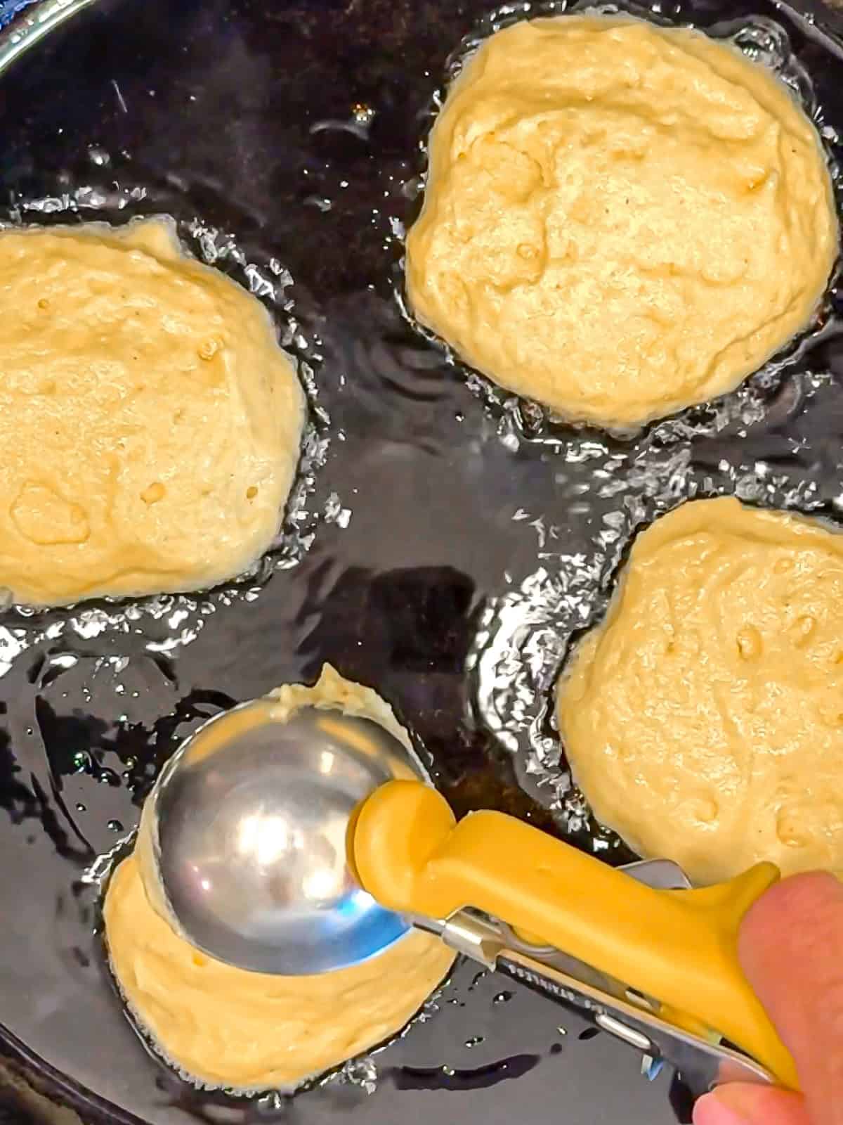 Placing cornbread batter into hot oil to make cupcakes.