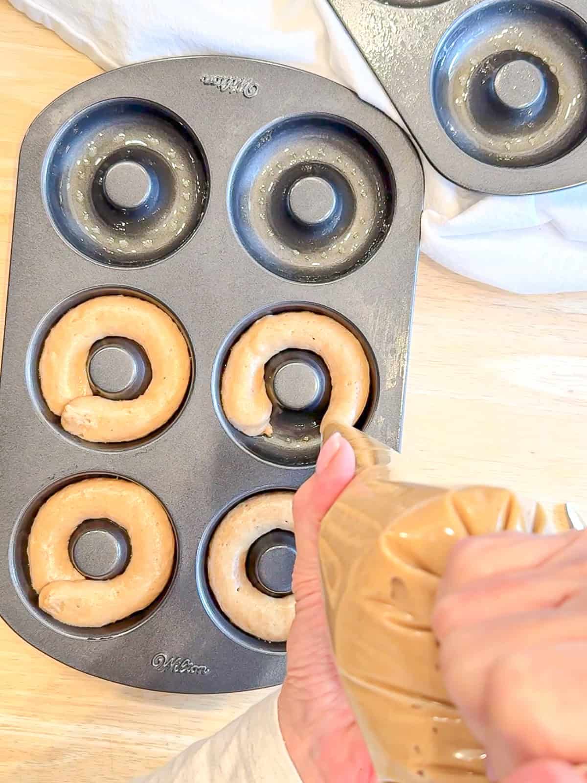 Piping donut batter into a donut pan.