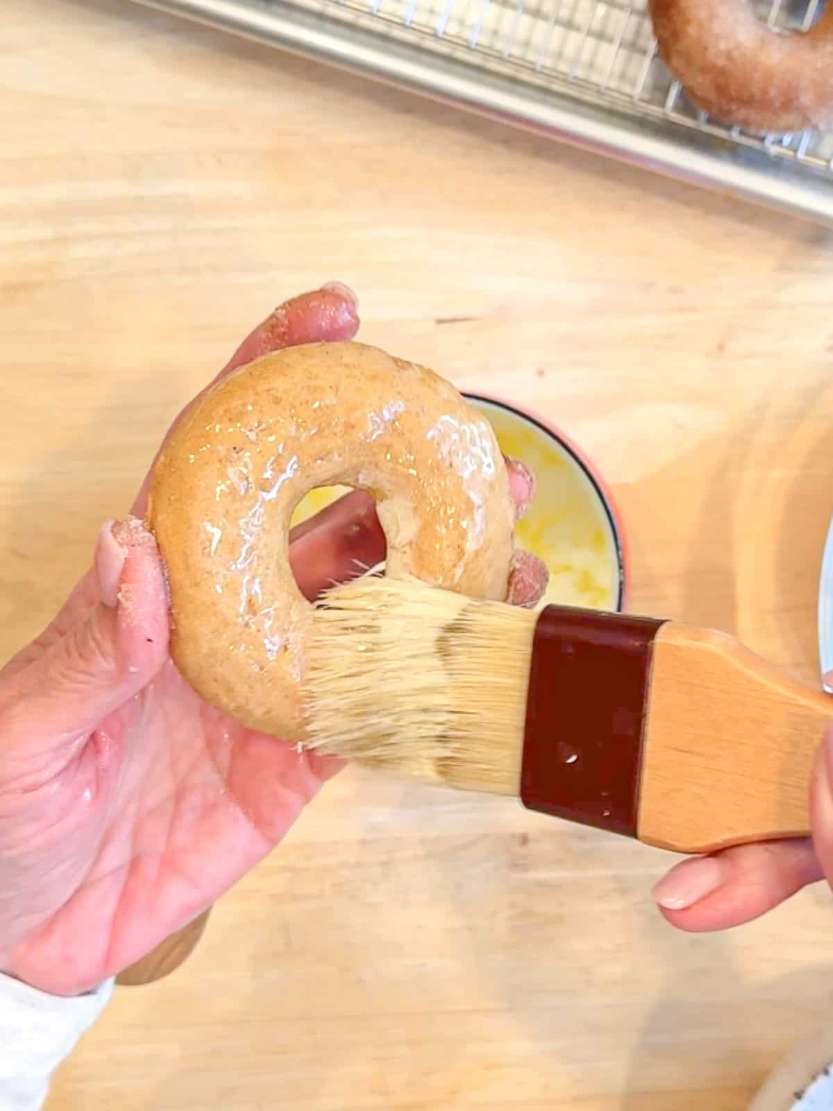 Brushing a baked apple cider donut with melted butter.