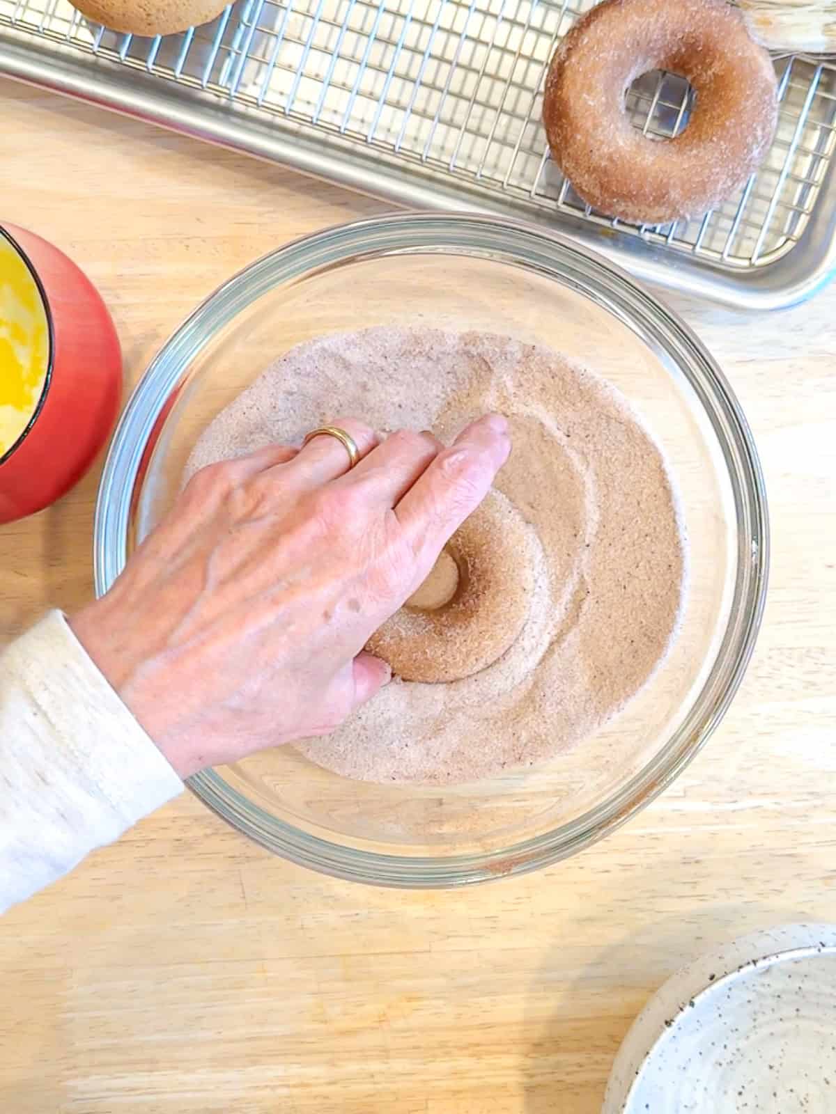 Rolling a baked apple cider donut in cinnamon sugar.