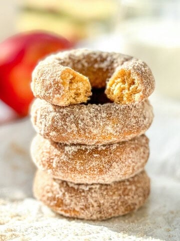 A stack of baked apple cider donuts, the one on top with a bite taken out.