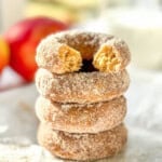 A stack of baked apple cider donuts, the one on top with a bite taken out.