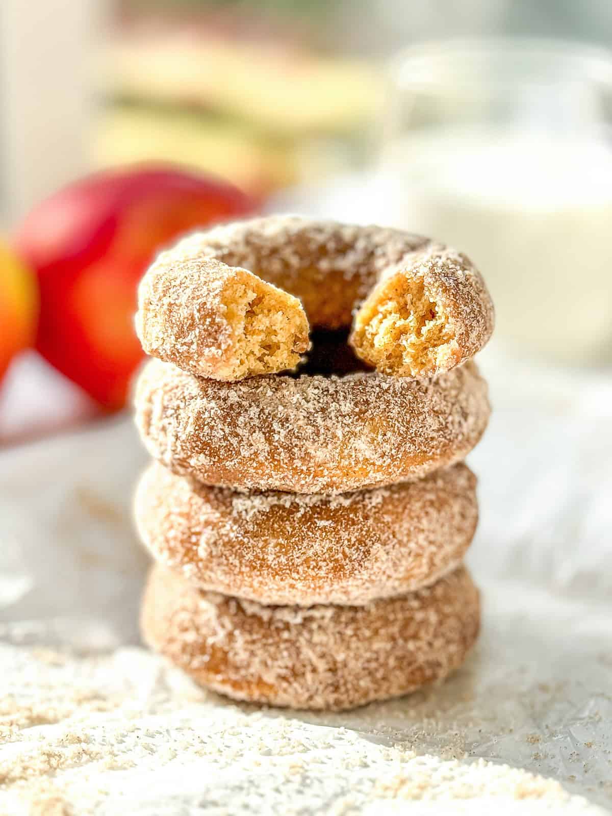 A stack of baked apple cider donuts, the one on top with a bite taken out.