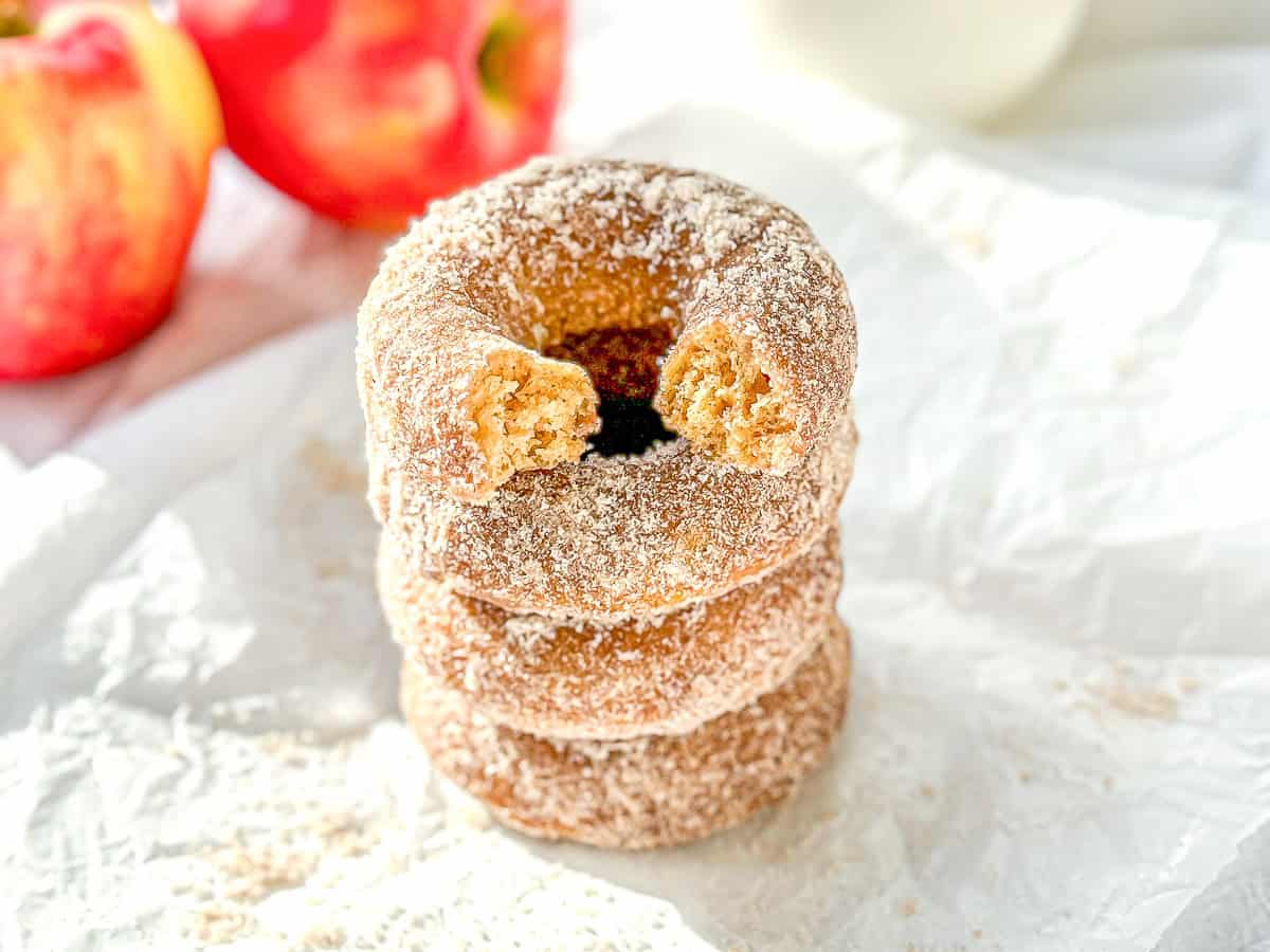 A stack of baked apple cider donuts, the one on top with a bite taken out.