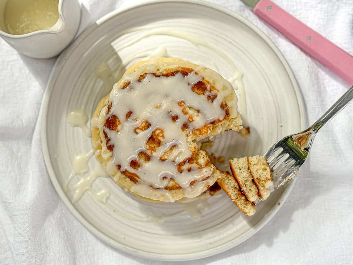 Using a fork to take a bite of a stack of cinnamon roll pancakes with cream cheese glaze.