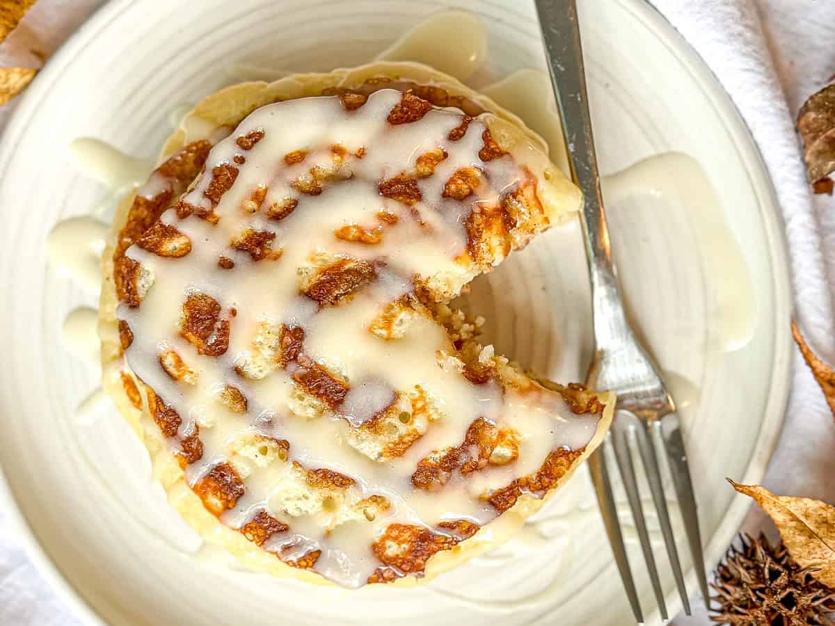 Cinnamon roll pancakes with cream cheese glaze on a white plate.