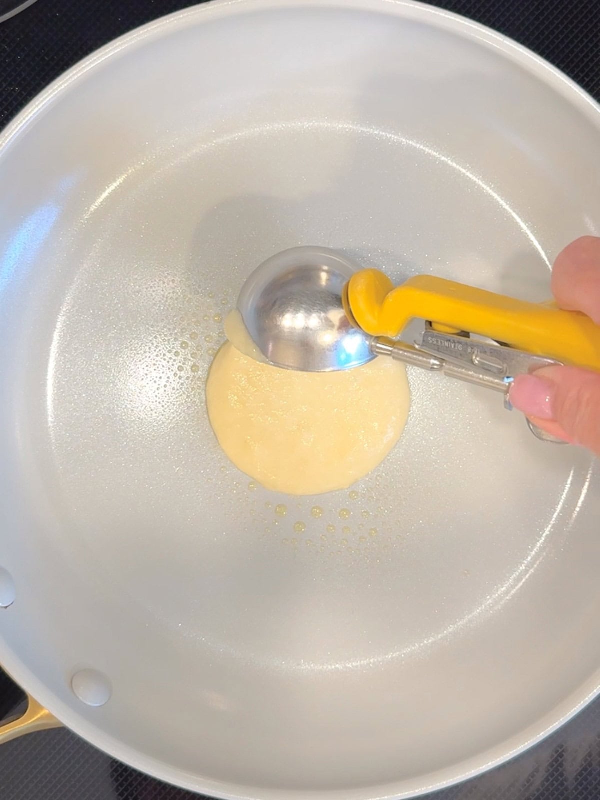 Adding a scoop of pancake batter to a nonstick pan.