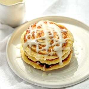 A stack of cinnamon roll pancakes with cream cheese glaze on a white plate.