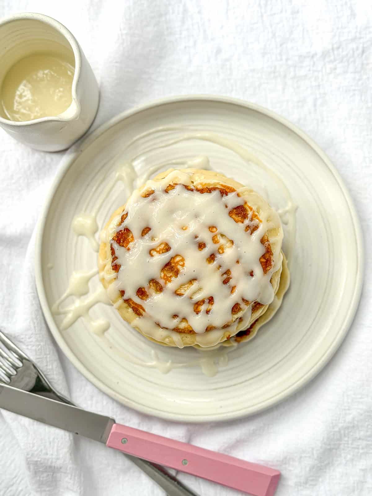 A stack of cinnamon roll pancakes with cream cheese glaze on a white plate.