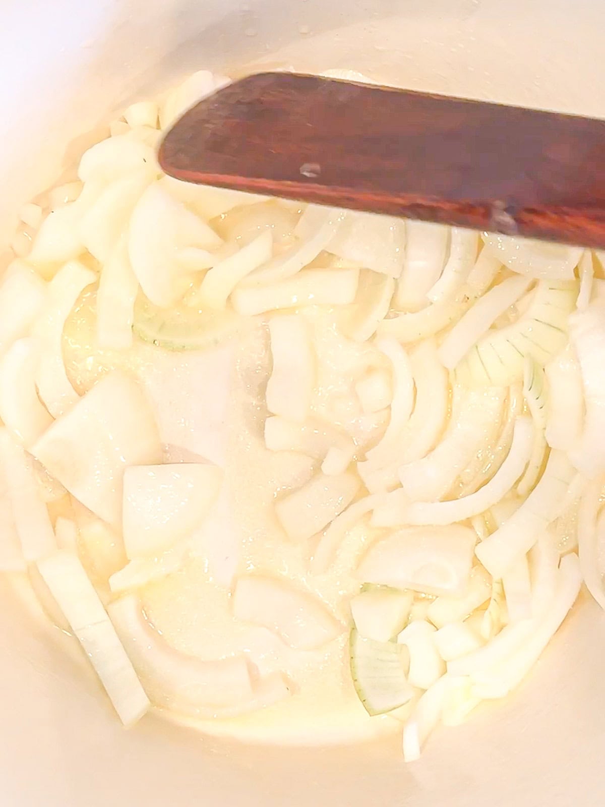 Sautéing onions in a white cast-iron Dutch oven.