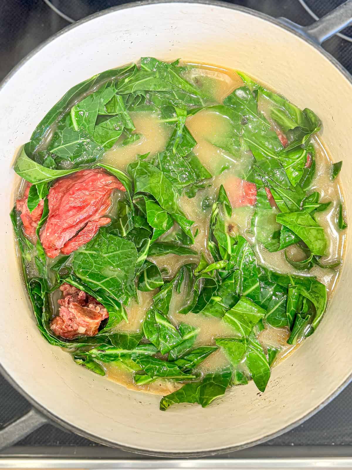 A cast-iron Dutch oven filled with collard greens with smoked pork.