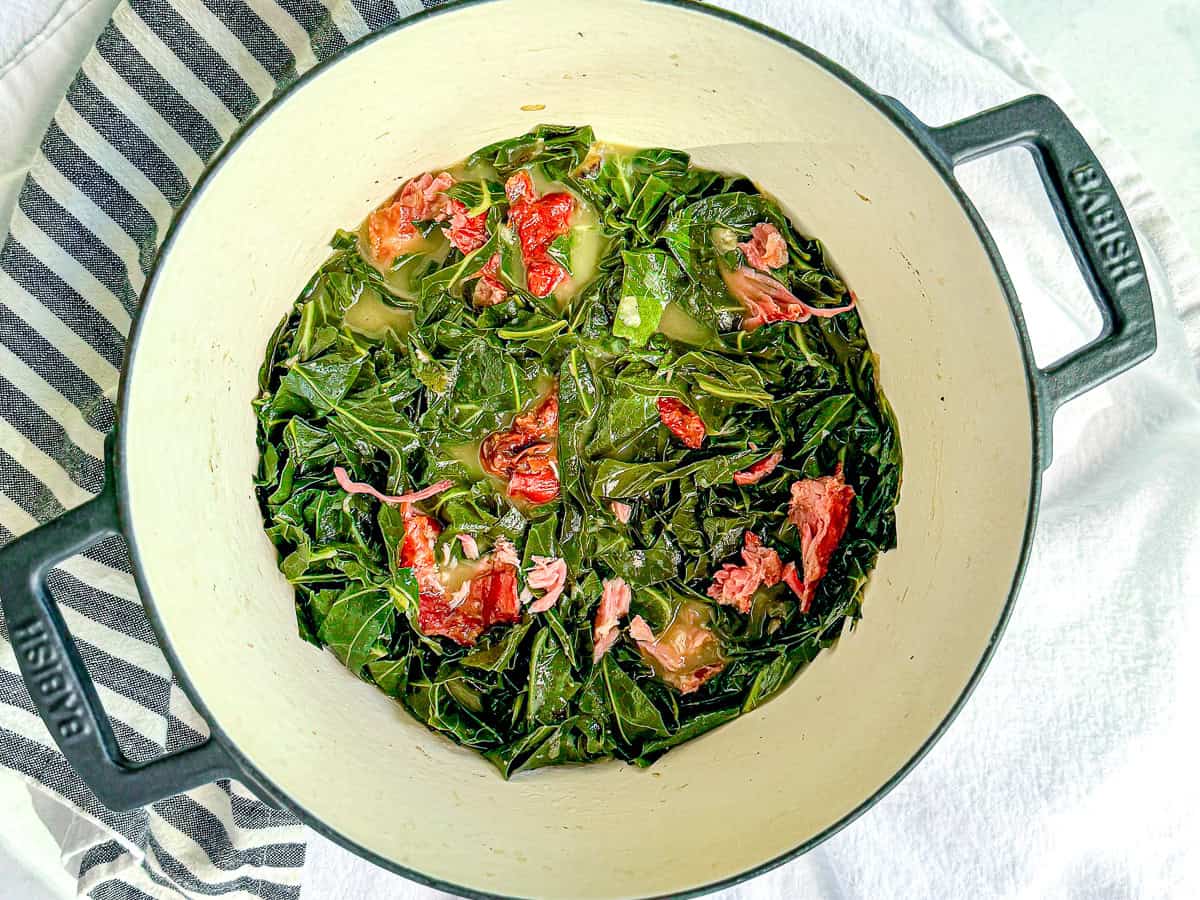 A cast-iron Dutch oven filled with collard greens with smoked pork.