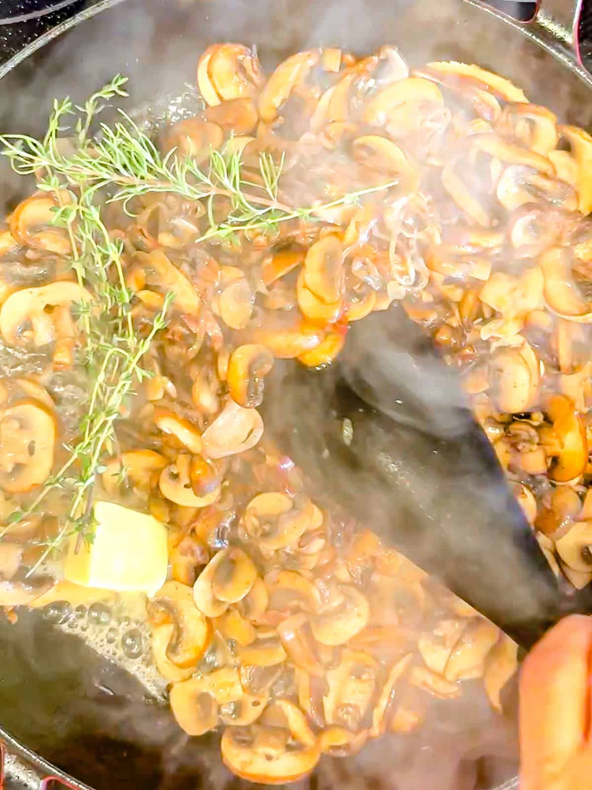 Sautéing mushrooms and shallots with fresh herbs in a skillet.