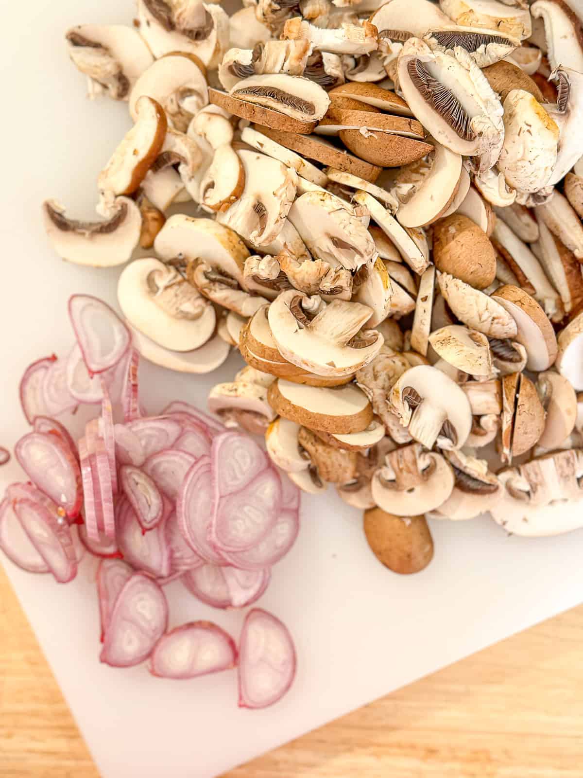 Sliced shallots and mushrooms on a white cutting board.