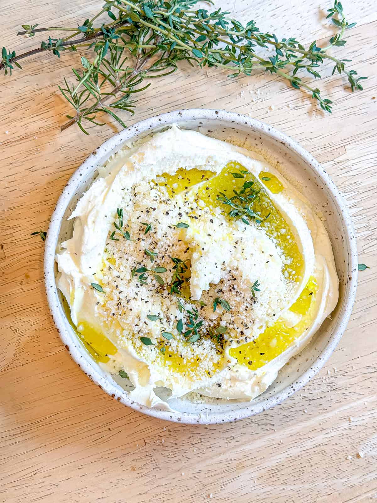 Mixing mascarpone, parmesan, olive oil, and herbs andf spices in a white bowl.