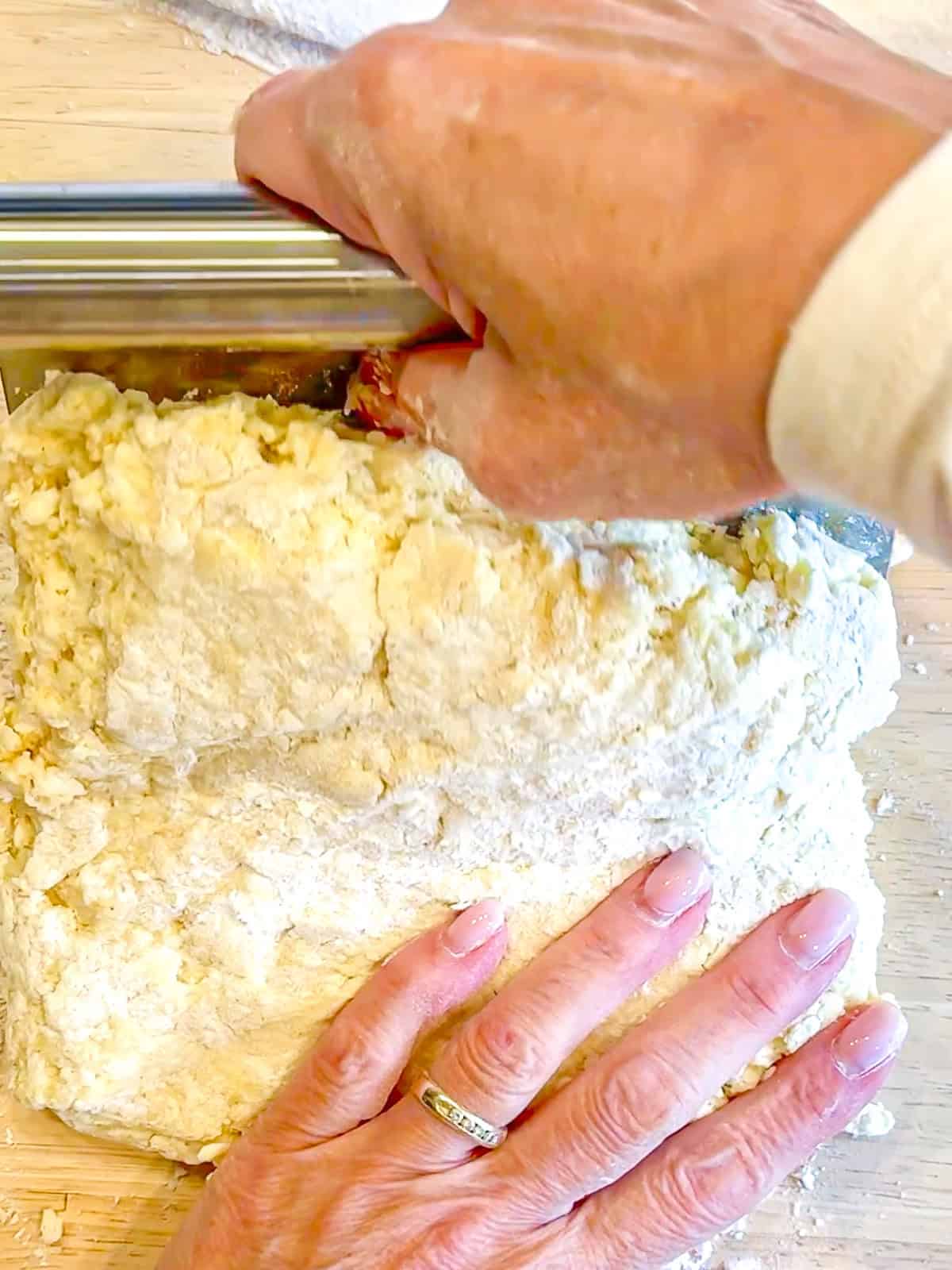 Using a bench scraper to fold, buttermilk scone over onto itself.