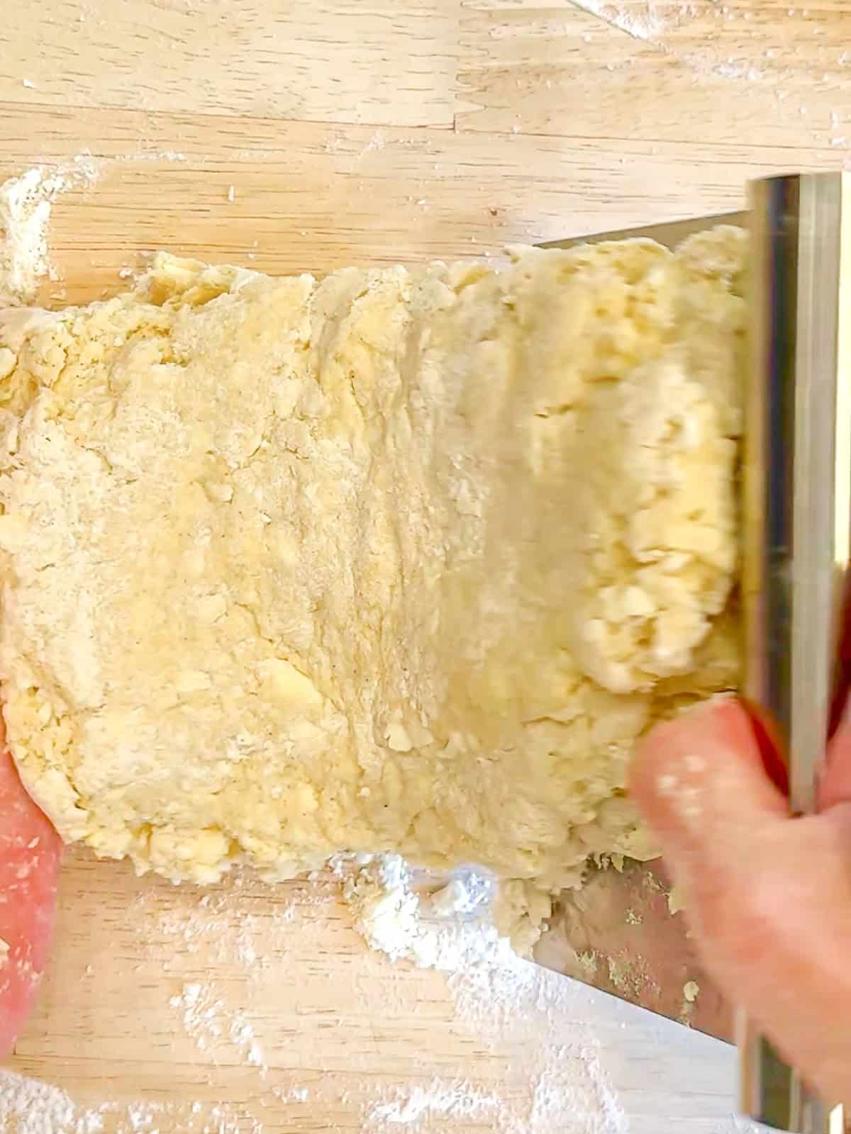 Using a bench scraper to fold, buttermilk scone over onto itself.