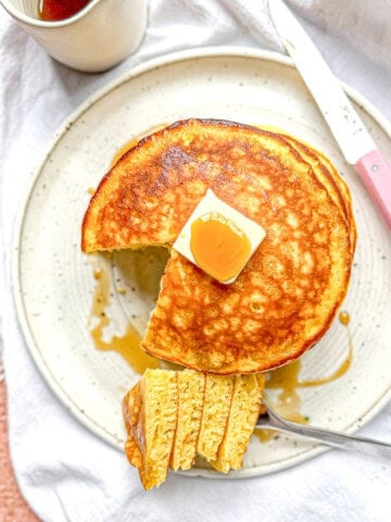 Eggnog pancakes on a white plate with a portion of pancakes on a fork.