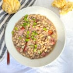 Southern black-eyed peas in a white bowl with a biscuit nearby.
