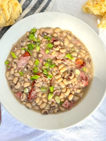 Southern black-eyed peas in a white bowl with a biscuit nearby.