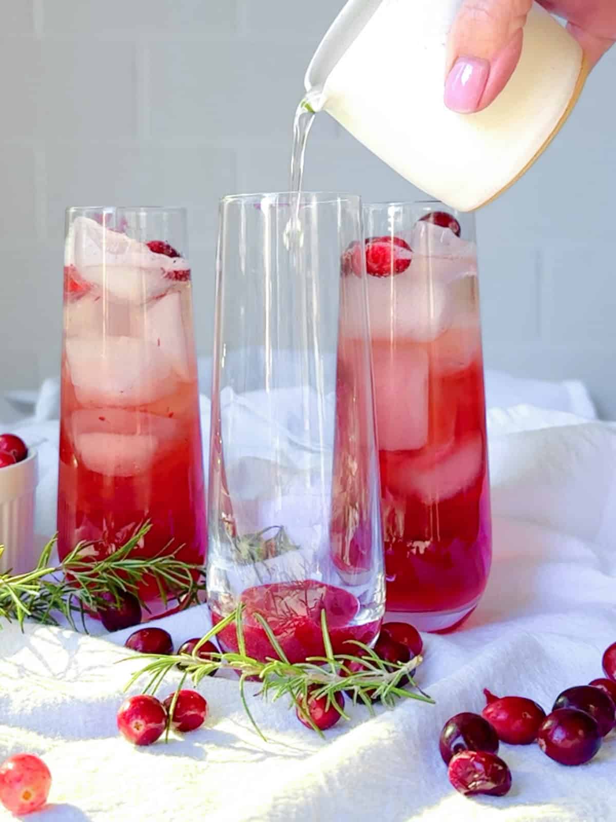 Pouring rosemary simple syrup into a glass for a cranberry mocktail.