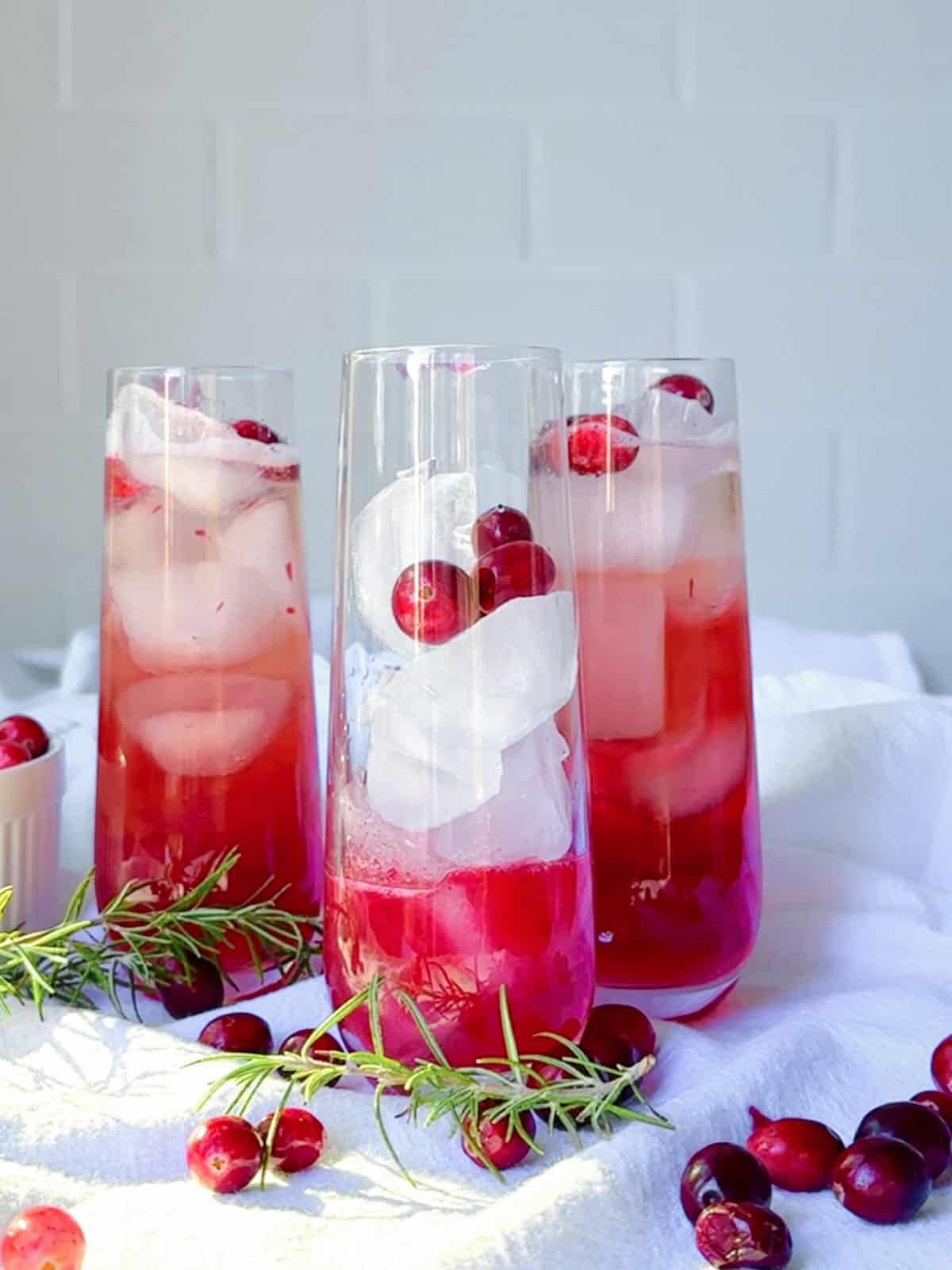 Adding ice and cranberries to a glass for a cranberry mocktail.