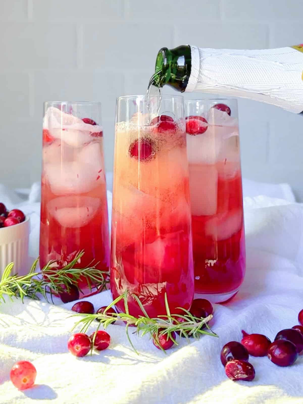 Pouring sparkling cider into a cranberry mocktail.