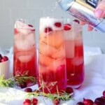 Pouring sparkling water into a cranberry mocktail.