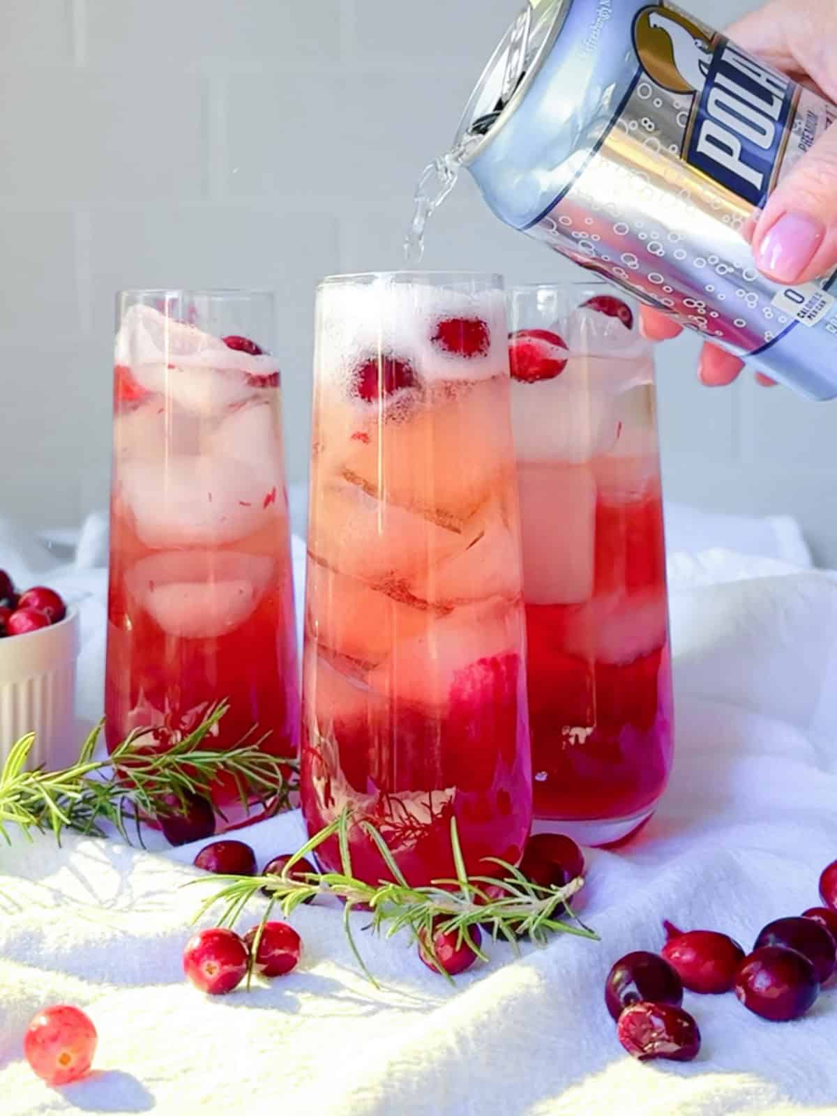 Pouring sparkling water into a cranberry mocktail.