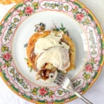 Cutting into a biscuit cinnamon roll on a flowered plate with a fork.