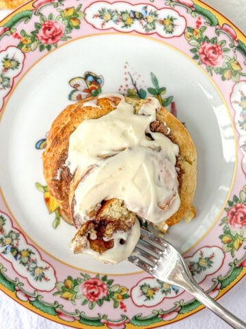 Cutting into a biscuit cinnamon roll on a flowered plate with a fork.