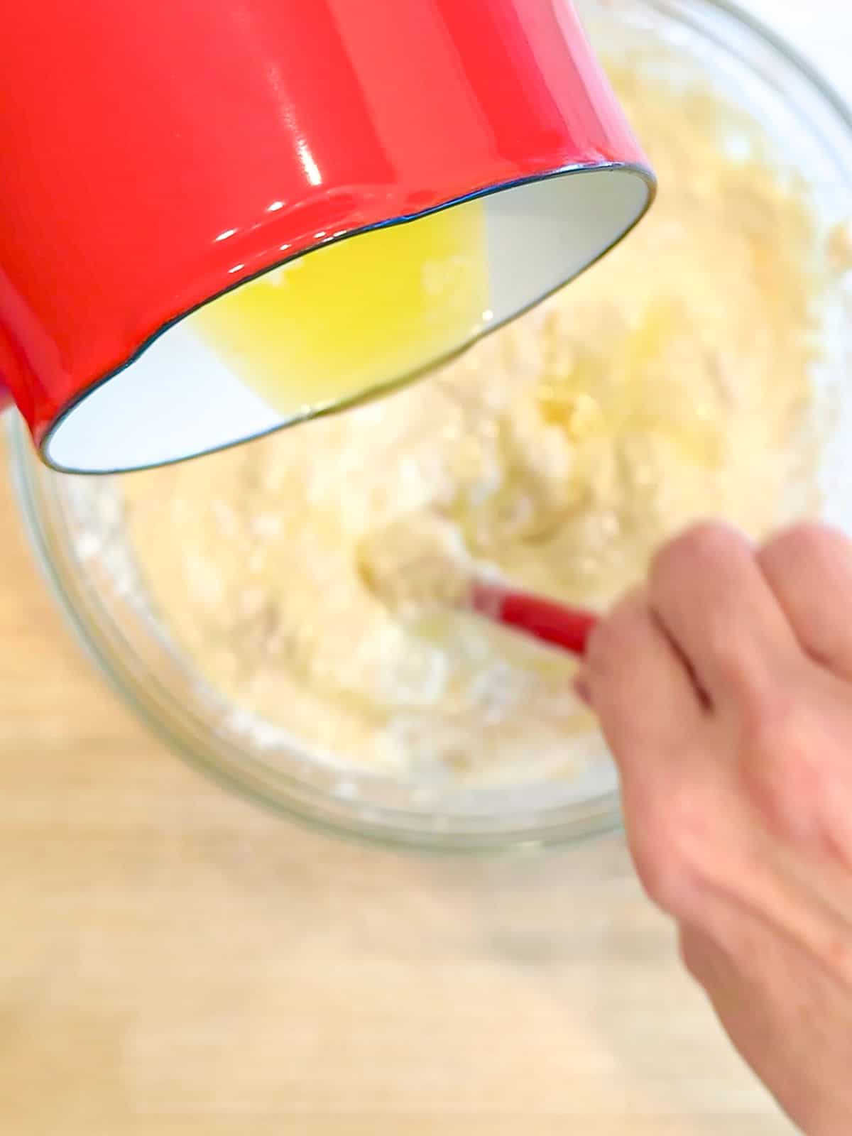 Mixing pancake batter while drizzling and melted and cooled butter.