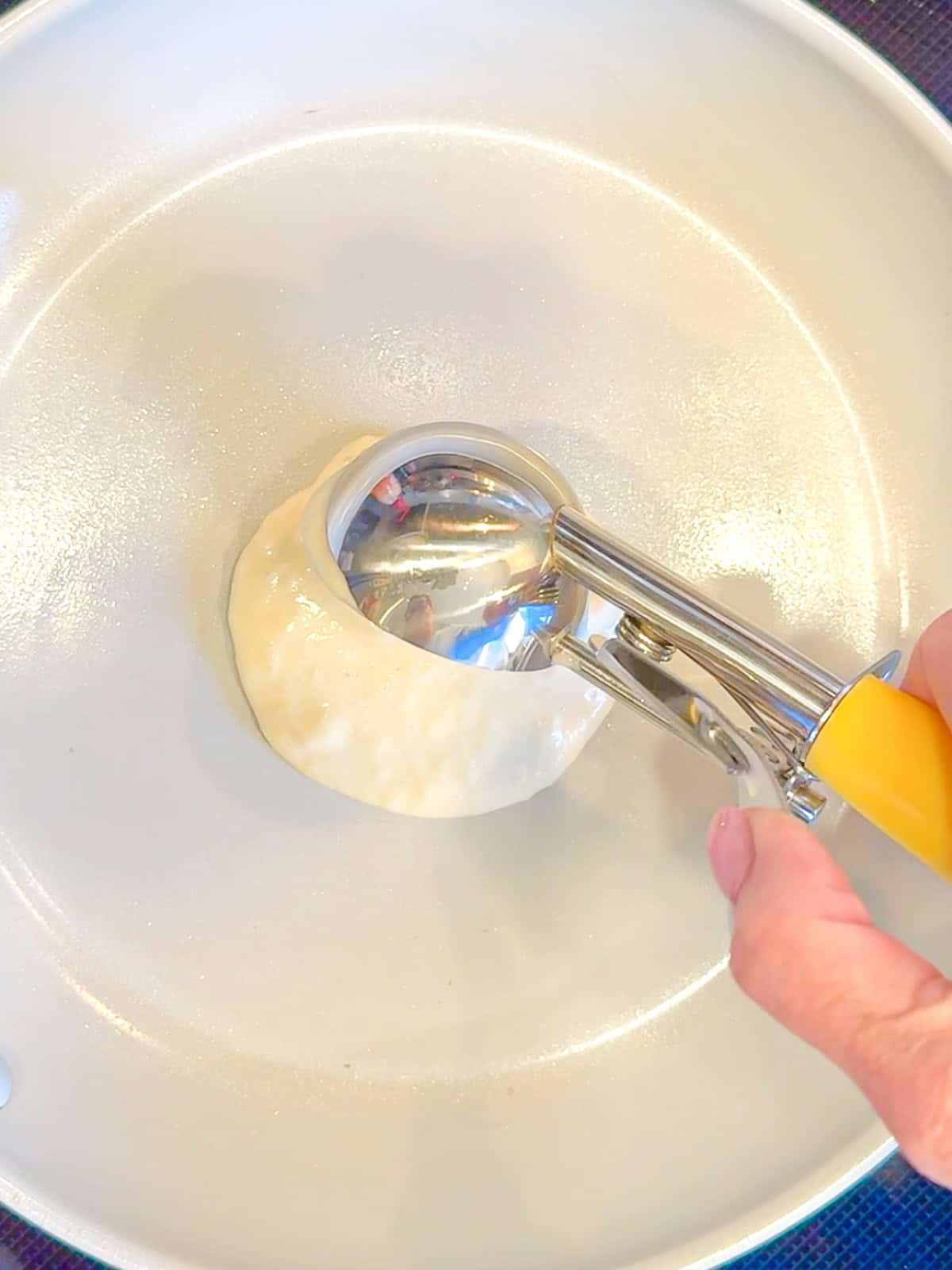 Using an ice cream scoop to Porsche and pancake batter onto a nonstick pan.