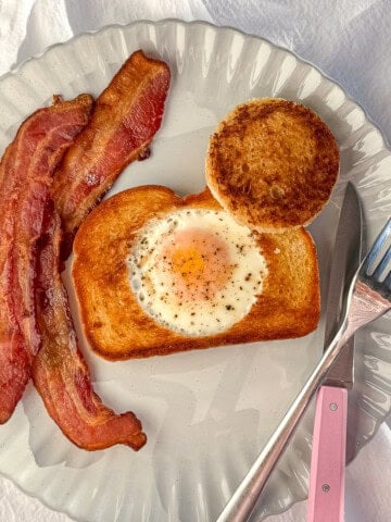 Egg in a hole on a gray plate with pieces of bacon.