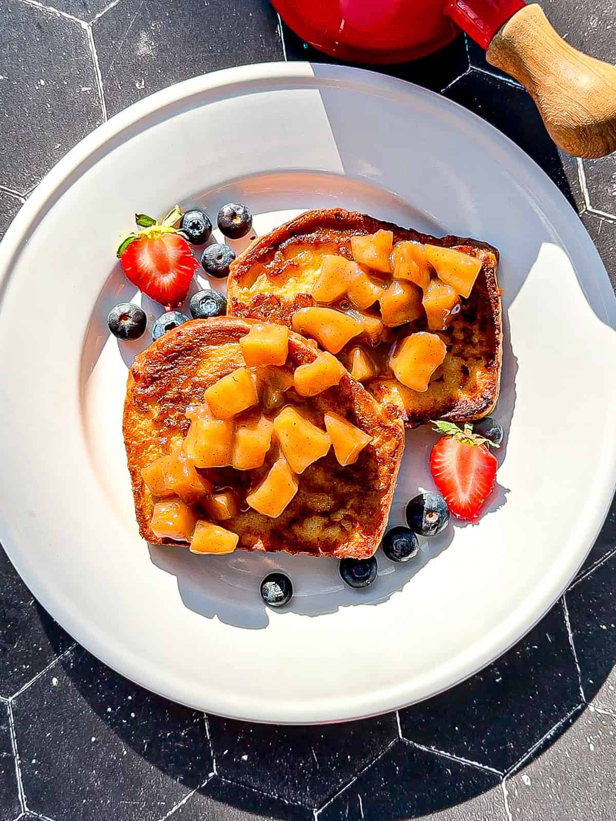 Granola with sautéed apples, maple syrup, and fresh fruit on a white plate.