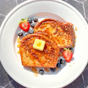 Two slices of French toast with fruit on a white plate.