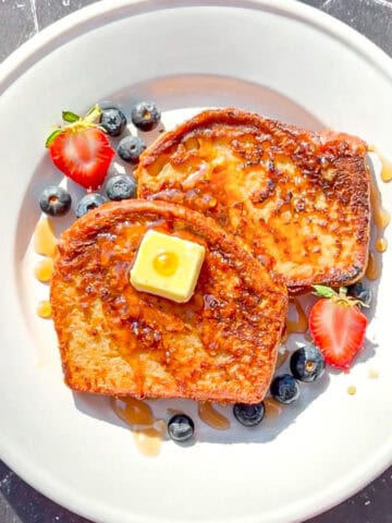 Two slices of French toast with fruit on a white plate.