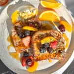 Orange French toast with fresh fruit and yogurt cream on a white plate.