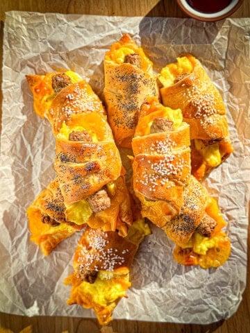 Sausage crescent rolls on a cutting board with a bowl of ketchup.